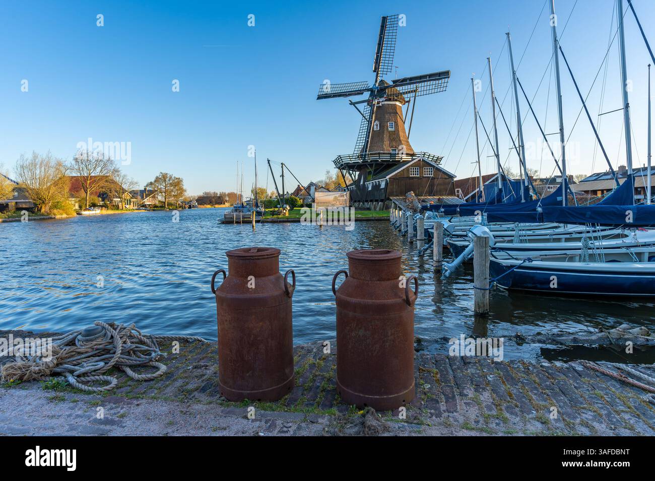 Typisch niederländische Landschaft mit zwei alten rostigen Milchkannen und der historischen Windmühle im Dorf Woudsend in der Provinz Friesland Stockfoto