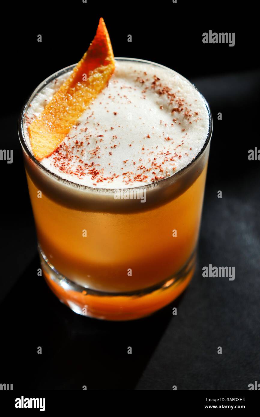Nahaufnahme eines klassischen Whiskey-Sour-Cocktails, garniert mit schaumigem Eiweißschaum und garniert mit einer frischen Orangenschale, serviert in einem klaren Glas Stockfoto