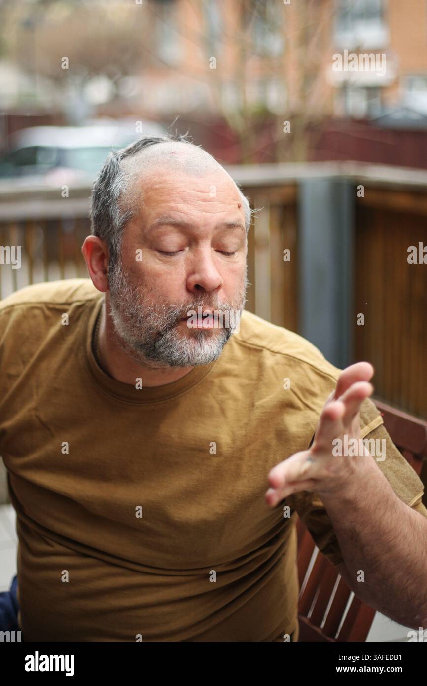 Seniorenmann mit geschlossenen Augen und erhobener Hand, humorvoller Moment während der Pflege Stockfoto