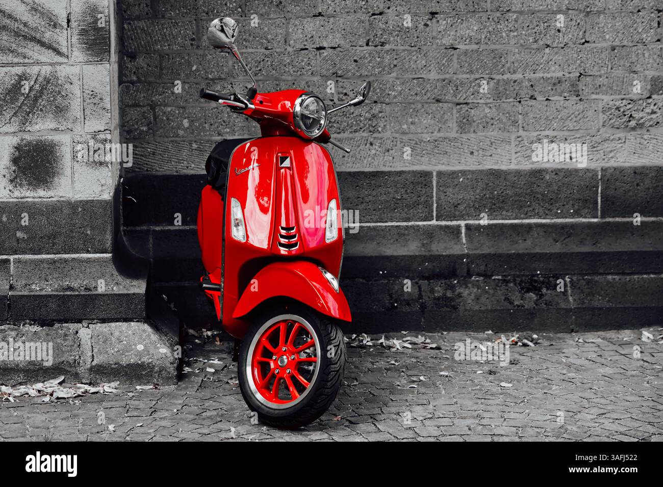 Ein leuchtend roter Vespa-Roller parkt vor der ikonischen Steinmauer des Kölner Doms in Köln, Deutschland, und zeigt gotische Architektur Stockfoto