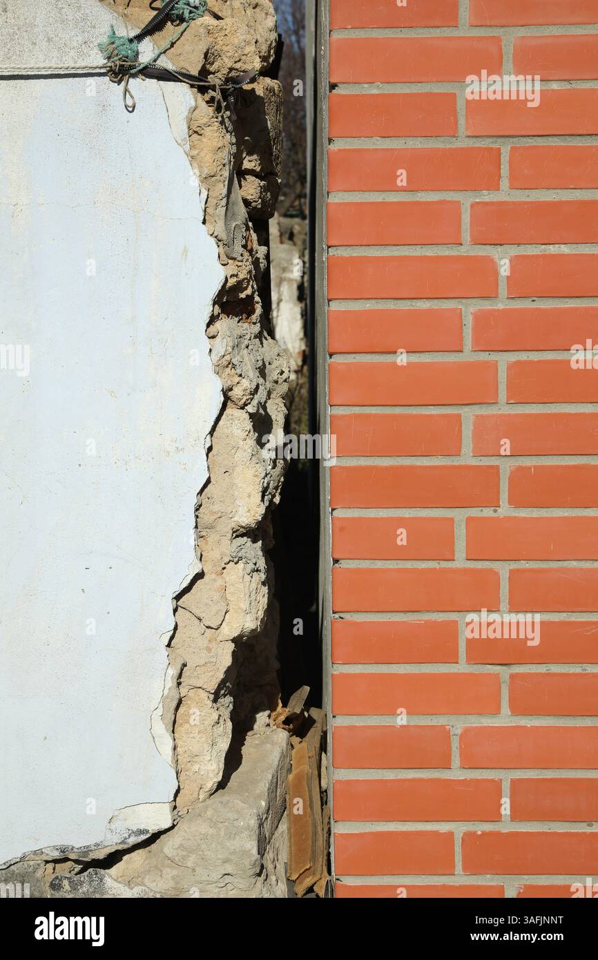 Altes weißes Gebäude in der Nähe einer neuen Backsteinmauer. Erdbeben nach dem Erdbeben Stockfoto
