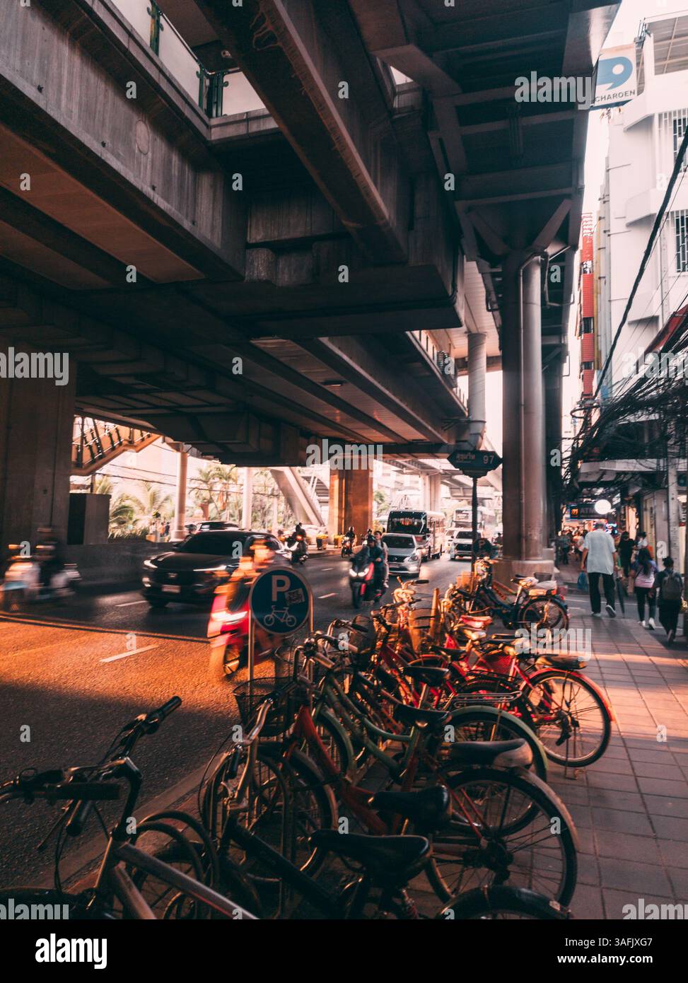 Erleben Sie Bangkoks pulsierendes Stadtleben mit dieser urbanen Straßenszene mit Fahrrädern, belebtem Verkehr, hohen Überführungen und dynamischer Energie Stockfoto
