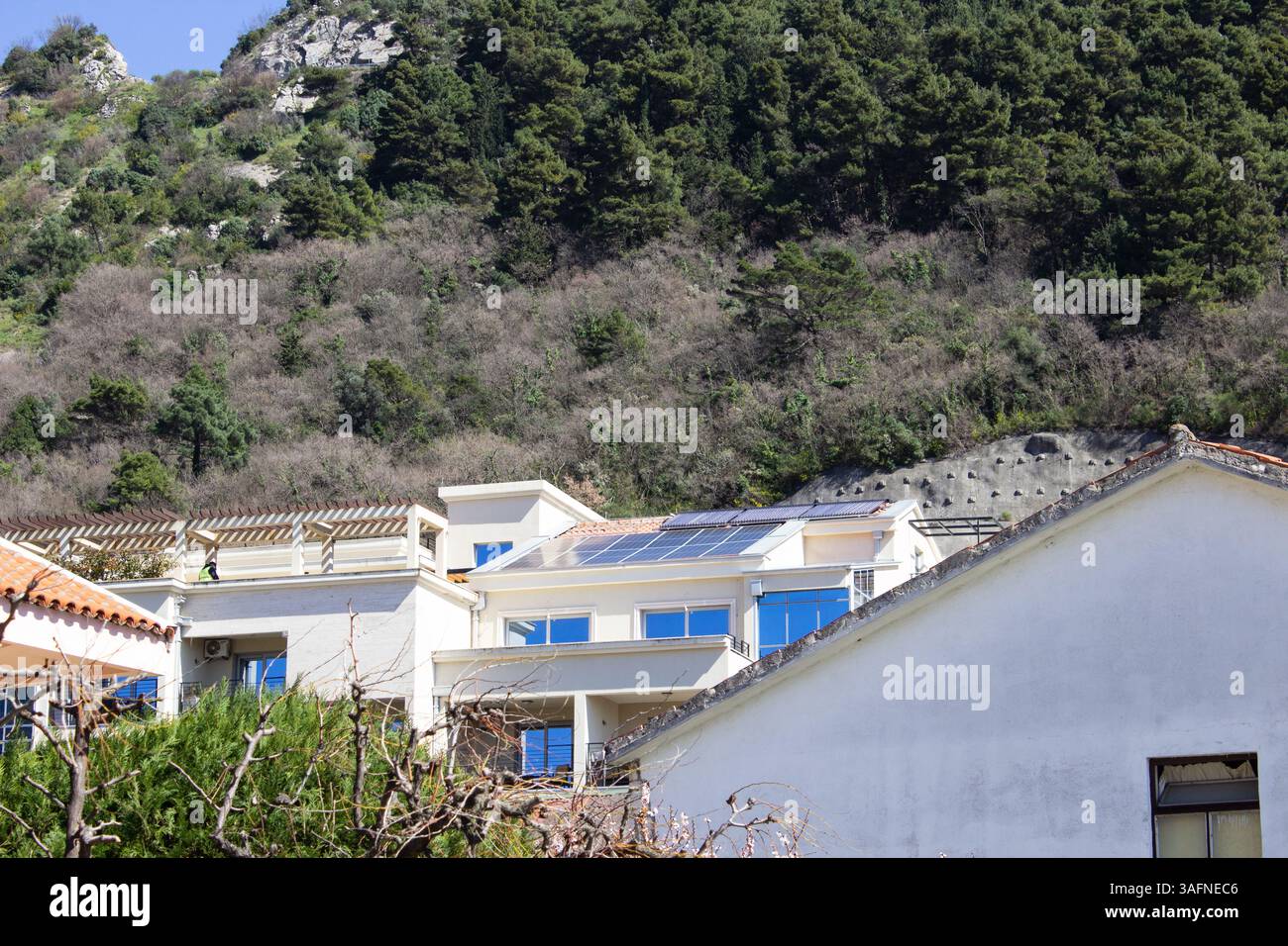 Weißes Öko-Haus mit Solarpaneelen und blauen Fensterrahmen in der Nähe der Küstenklippe. Nachhaltige Architektur in Montenegro Stockfoto