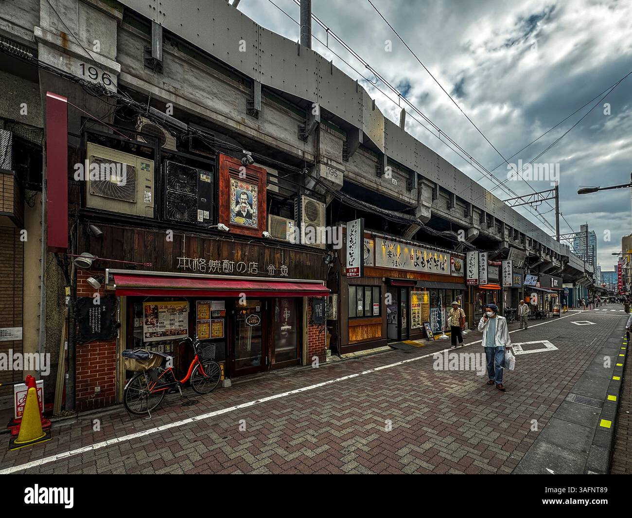 Eine ruhige Straße mit Geschäften und Restaurants, die unter Hochbahnlinien in Tokio, Japan, gebaut wurden - Smartphone-aufgenommenes Stockfoto