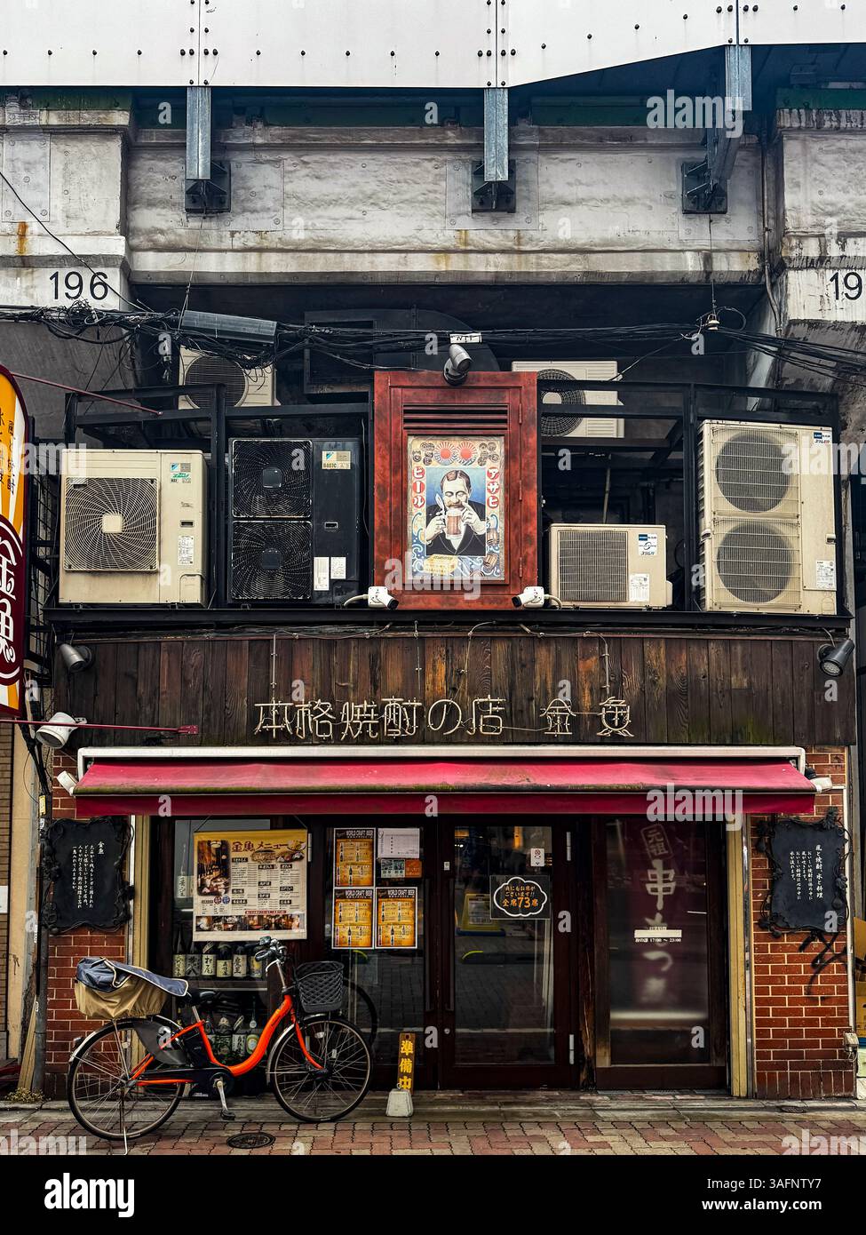 Eine ruhige Straße mit Geschäften und Restaurants, die unter Hochbahnlinien in Tokio, Japan, gebaut wurden - Smartphone-aufgenommenes Stockfoto