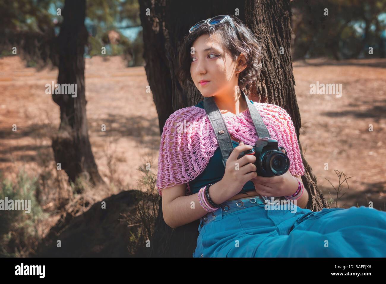 Junge Fotografin, die eine professionelle Kamera hält, sitzt auf einem Baum in einem schönen Wald, Weltfotografie Tag Konzept, Kopierraum Stockfoto