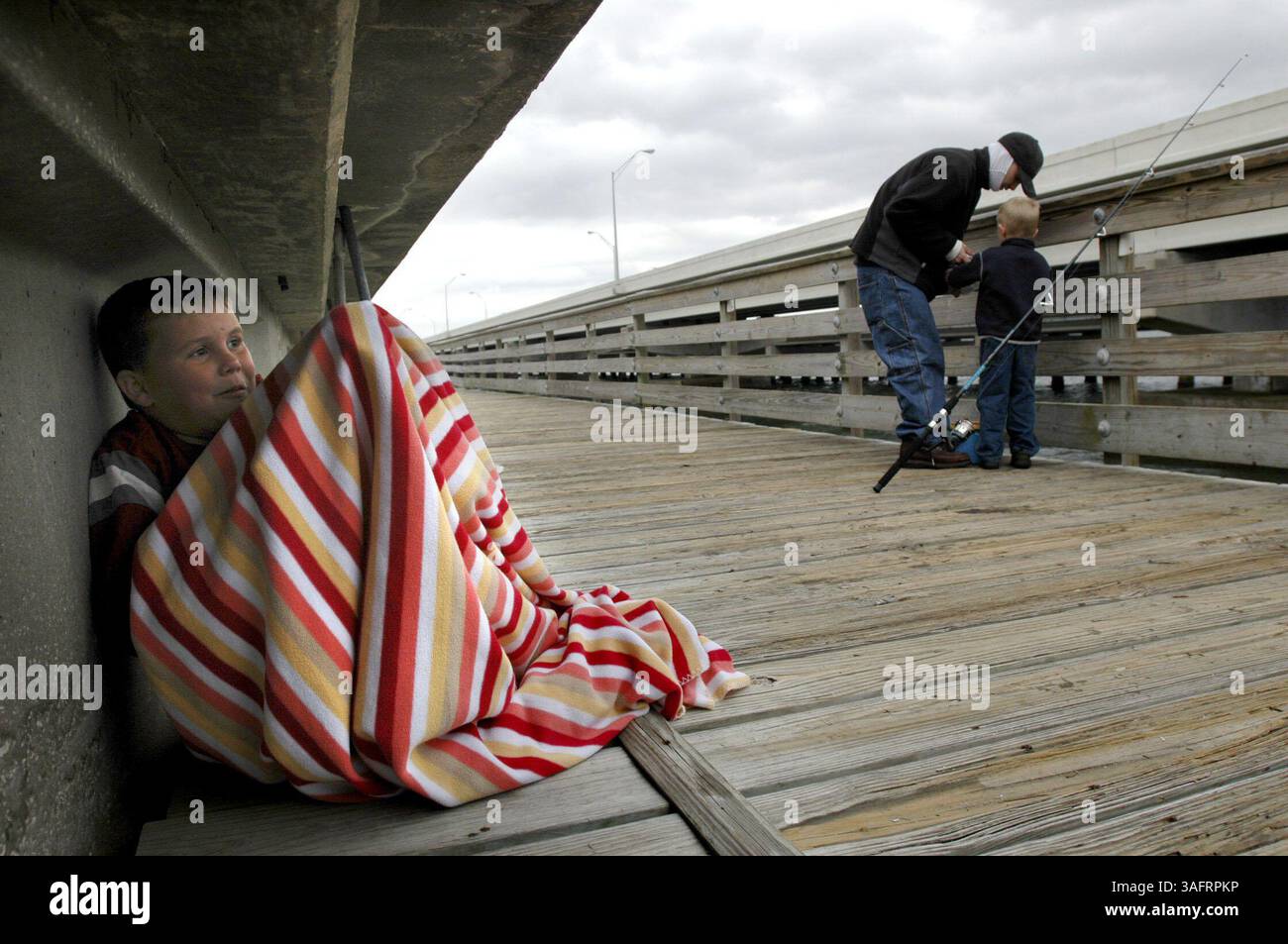 Bradley Summerlin, 8 Jahre alt, passt seine Decke an, um sich warm zu halten, als sein jüngerer Bruder Clay Summerlin, 4 Jahre alt, und ihr Vater, Jason Summerlin, 30, Fisch an einem unerwartet kalten Sonntagnachmittag an der Friendship Trail Bridge. Auf Wunsch von Clay, dessen 5. Geburtstag am Valentinstag ist, kam die Familie, einschließlich des älteren Bruders Jason Summerlin, 13, und Dads Freundin Jennifer Ayala, aus Winter Haven, um zum Angeln zu gehen. Trotz der Kälte und wenn man bedenkt, dass sie so weit gekommen waren und am Abend zuvor für ein Hotel bezahlt hatten, wollten sie ihn nicht im Stich lassen. ''Ich dachte nicht, dass es g war Stockfoto