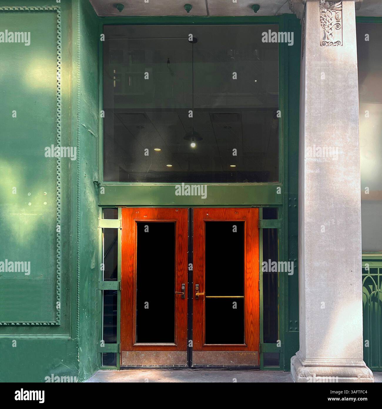 Gusseiserne grüne Fassade mit verzierten Details und einer großen Steinsäule, Rahmenholz- und Glasdoppeltüren in einem historischen Gebäude in Chicago - Smartphone-aufgenommenes Stockfoto