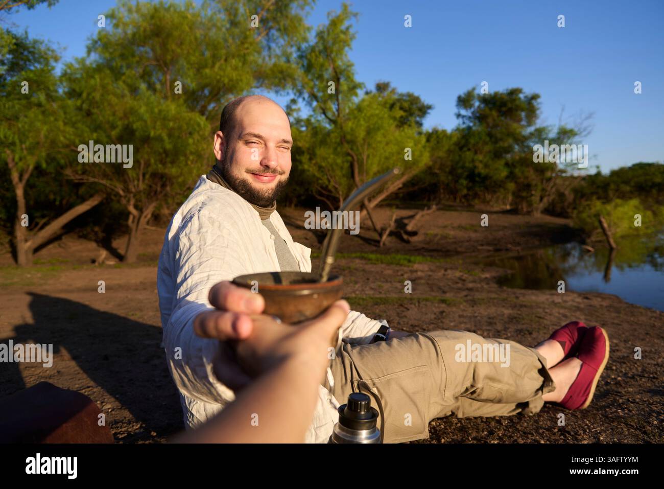 Ein lächelnder Mann trinkt mit jemandem. Dieser argentinische Aufguss ist ein Symbol für das Teilen und Zusammensein. Komposition mit selektivem Fokus. Stockfoto