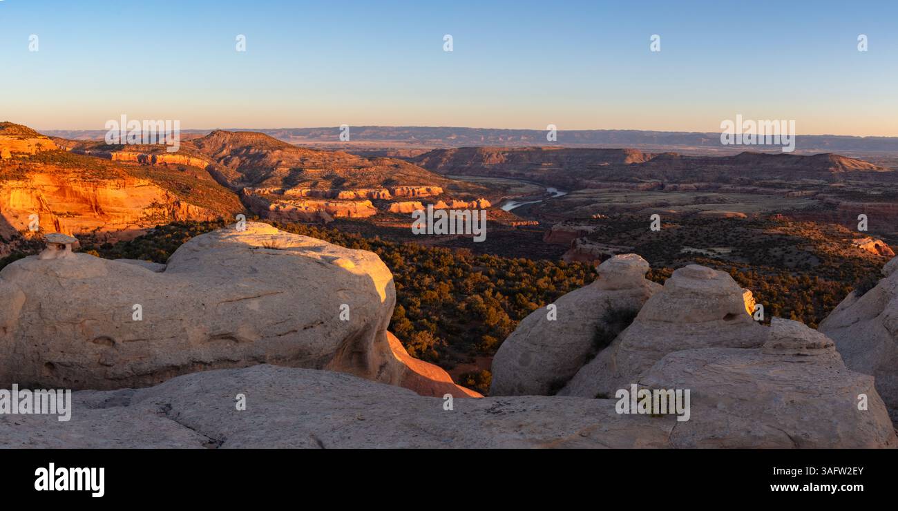 Der Colorado River bleibt im Schatten, während die Klippen und Berge morgens in der Nähe von Fruita Colorado warmes erstes Licht erleuchten. Stockfoto