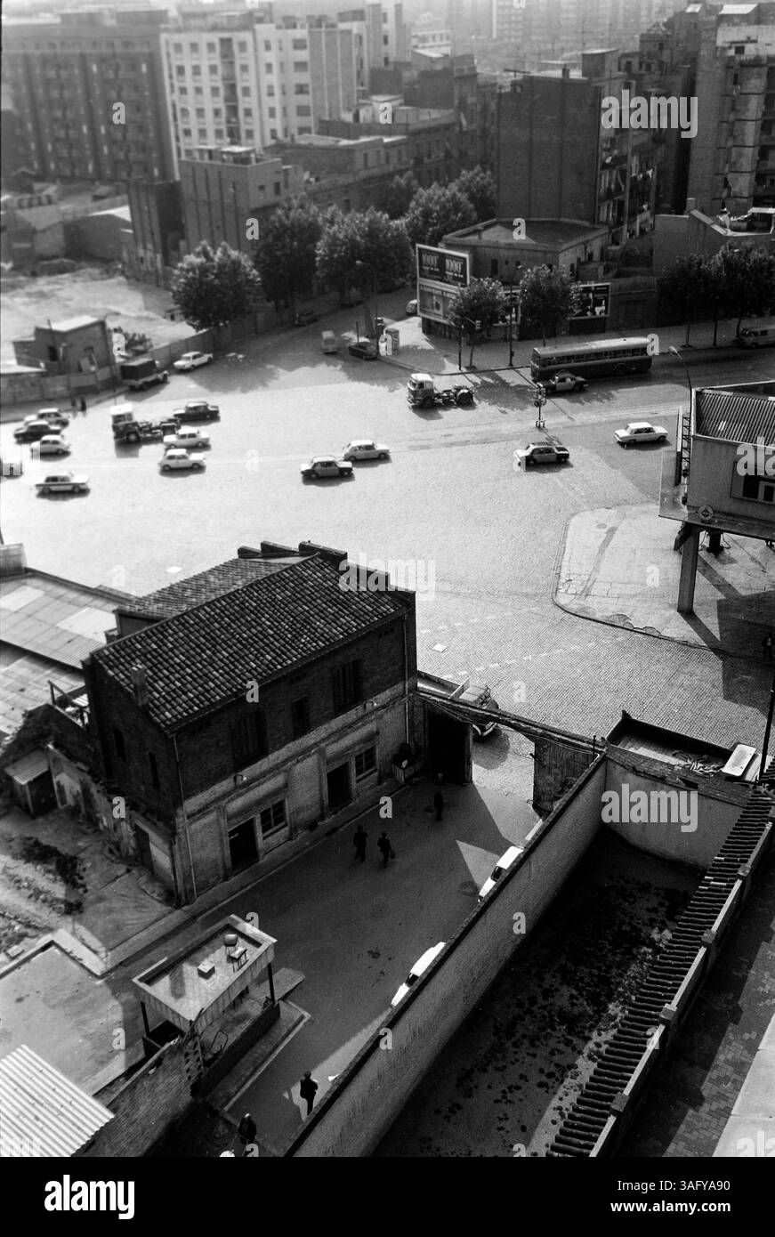 Blick auf den Hof eines zweistöckigen Wohn- und Geschäftshauses an einer Straßenkreuzung im Stadtteil Gràcia, im Hintergrund reihen sich mehrstöckige Wohnhäuser aneinander, Barcelona 1975. Blick auf den Innenhof eines zweistöckigen Wohn- und Geschäftshauses an einer Kreuzung im Stadtteil Gràcia, mit mehrstöckigen Wohnhäusern im Hintergrund, Barcelona 1975. Stockfoto