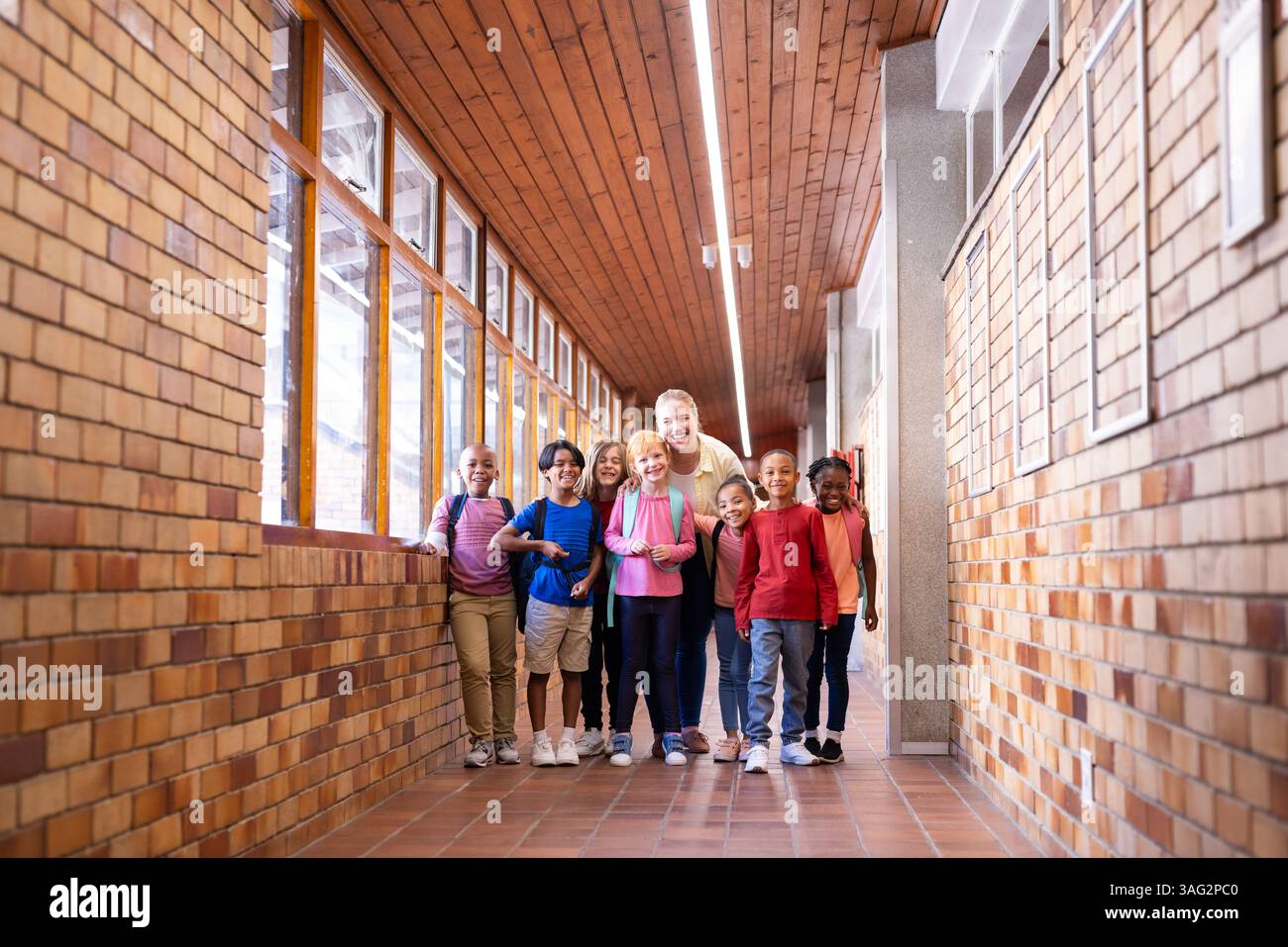 Lehrerin mit verschiedenen Schülergruppen, die im Schulflur stehen und lächeln Stockfoto