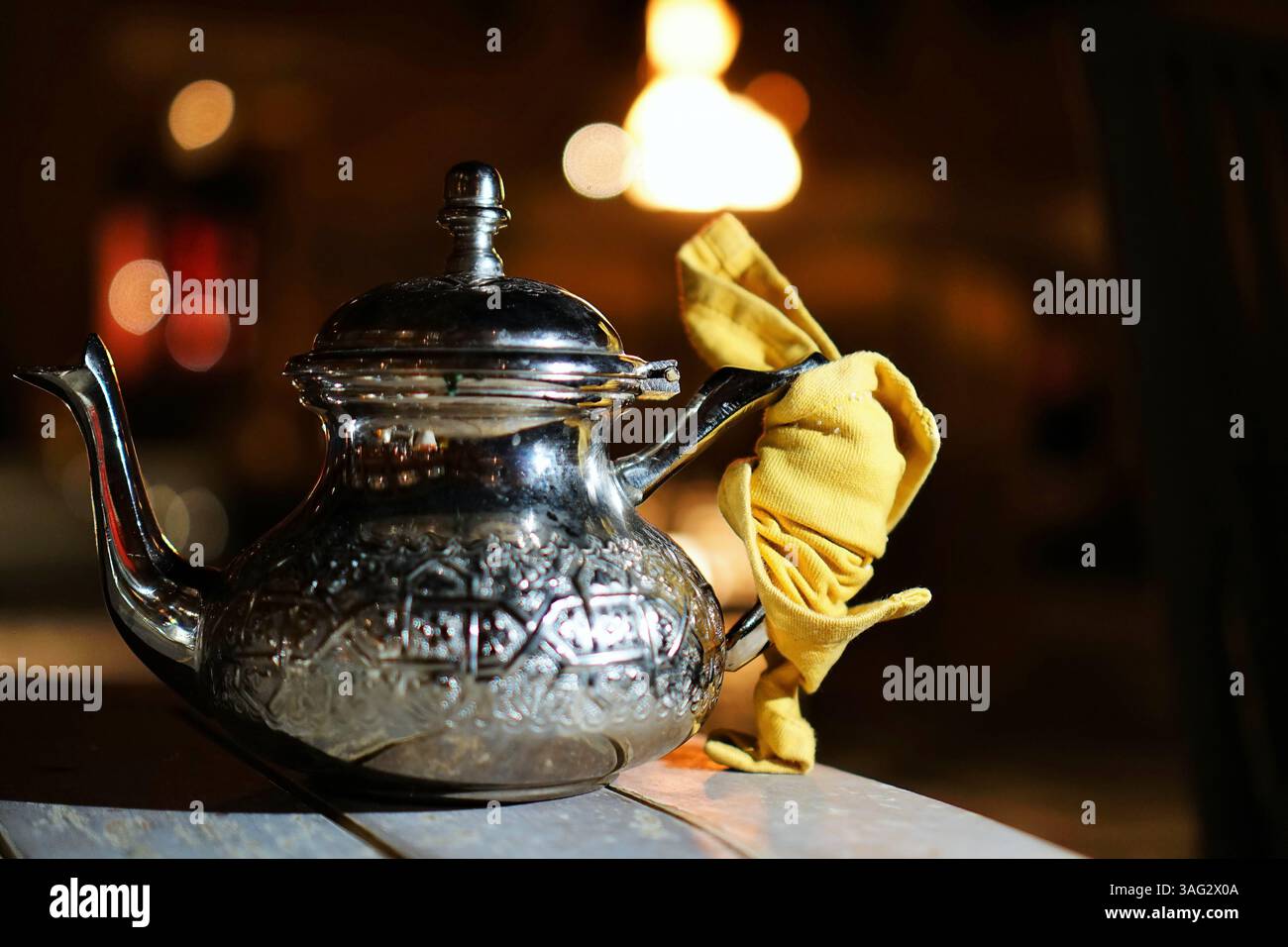 Dekorative Teekanne im nahöstlichen oder marokkanischen Stil mit graviertem Muster und Stoffgriff, warm beleuchtet in gemütlicher Atmosphäre Stockfoto