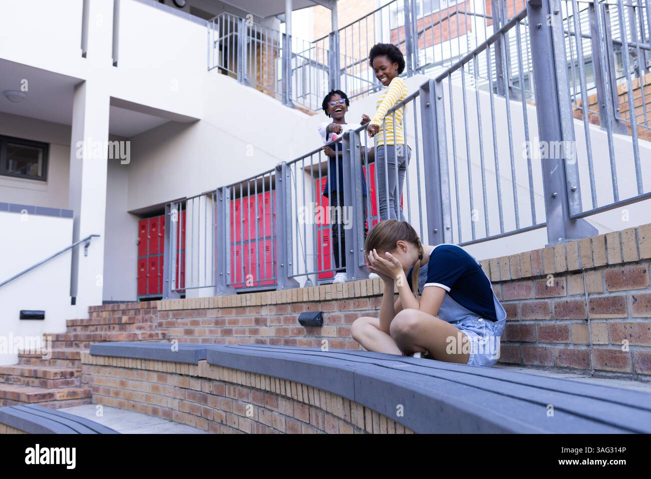 Weinendes Mädchen, das allein sitzt, während zwei afroamerikanische Kinder sie in der Schule auslachen Stockfoto