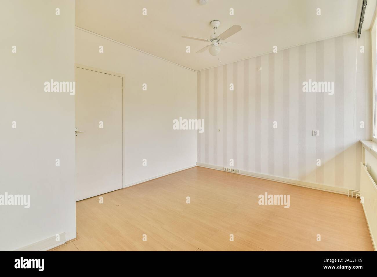 Helles, minimalistisches Zimmer mit hellem Holzfußboden, neutralen Wänden mit dezenten Streifen und natürlichem Licht durch das Fenster. Stockfoto