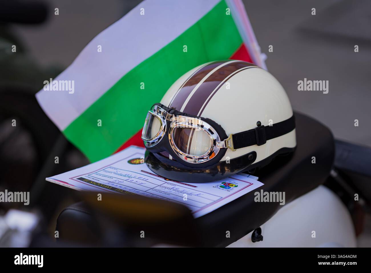 Motorradhelm im Retro-Stil mit Schutzbrille auf einem Vintage-Motorradsitz, begleitet von bulgarischer Flagge und Anmeldeformular. Zusammensetzung Stockfoto
