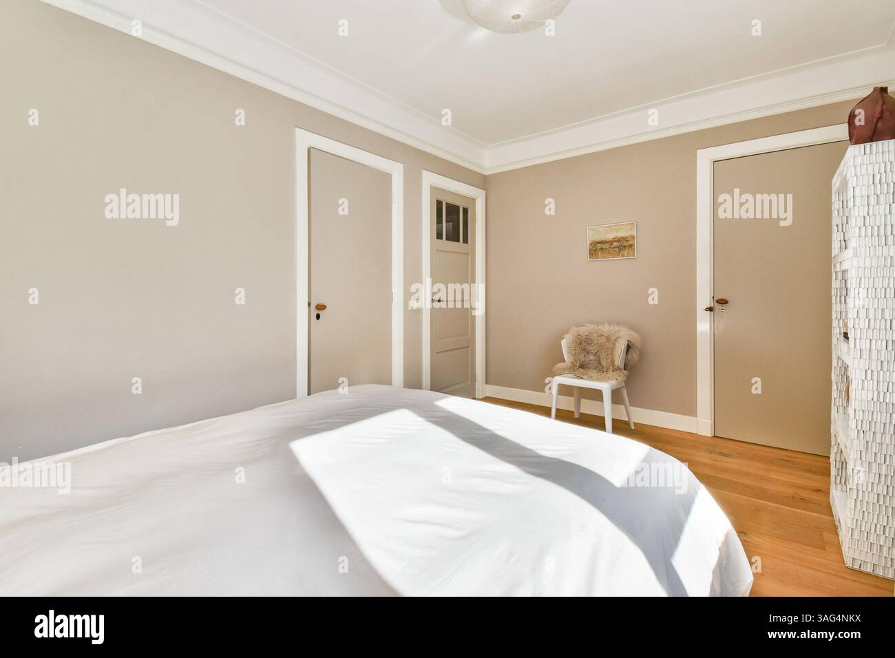 Ein gut beleuchtetes, minimalistisches Schlafzimmer mit weicher weißer Bettwäsche und Naturholzfußboden. Die Wände sind in neutralen Tönen gestrichen und sorgen für ein beruhigendes Ambiente. Stockfoto