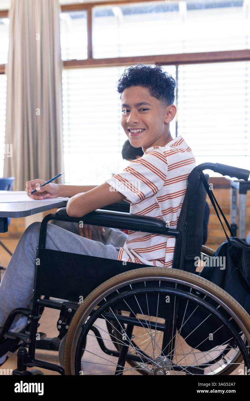 In der Schule lächelte ein Junge im Rollstuhl und schrieb im Klassenraum im Notizbuch Stockfoto