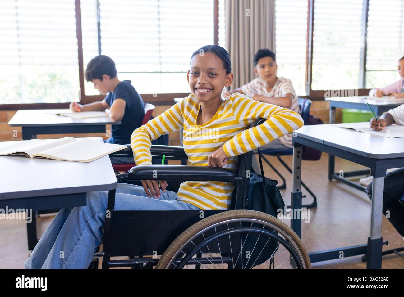 In der Schule lächelte ein Mädchen im Rollstuhl und lernte mit Klassenkameraden im Klassenzimmer Stockfoto