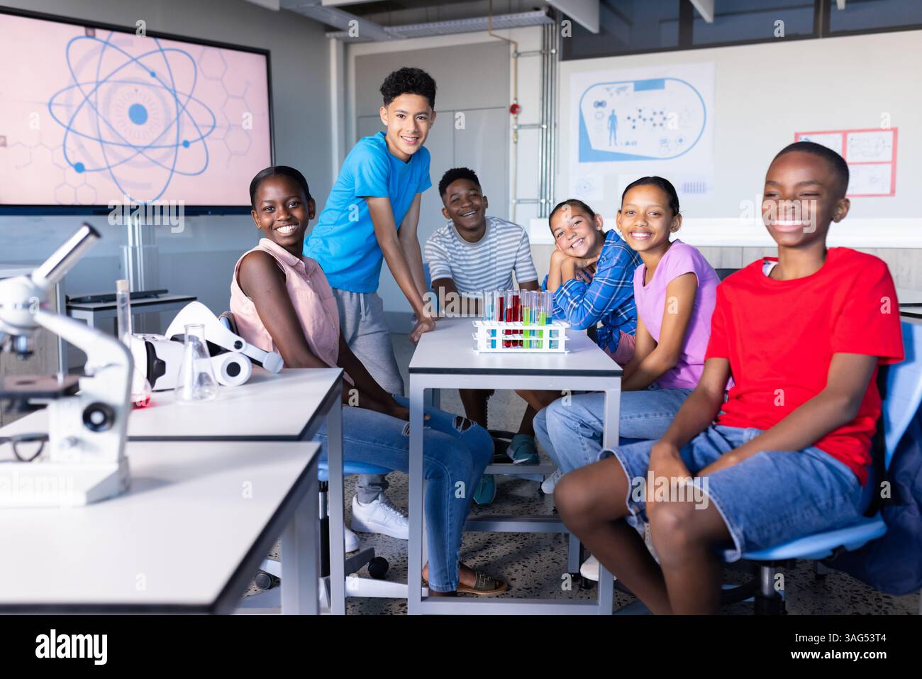 Im Wissenschaftslabor der Schule lächelte eine Gruppe von Schülern und saß um den Tisch Stockfoto