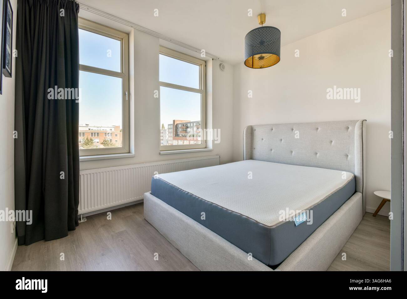 Ein helles, minimalistisches Schlafzimmer mit großen Fenstern und modernem Bettendesign. Die dezente Einrichtung und das Sonnenlicht schaffen ein ruhiges Ambiente. Stockfoto