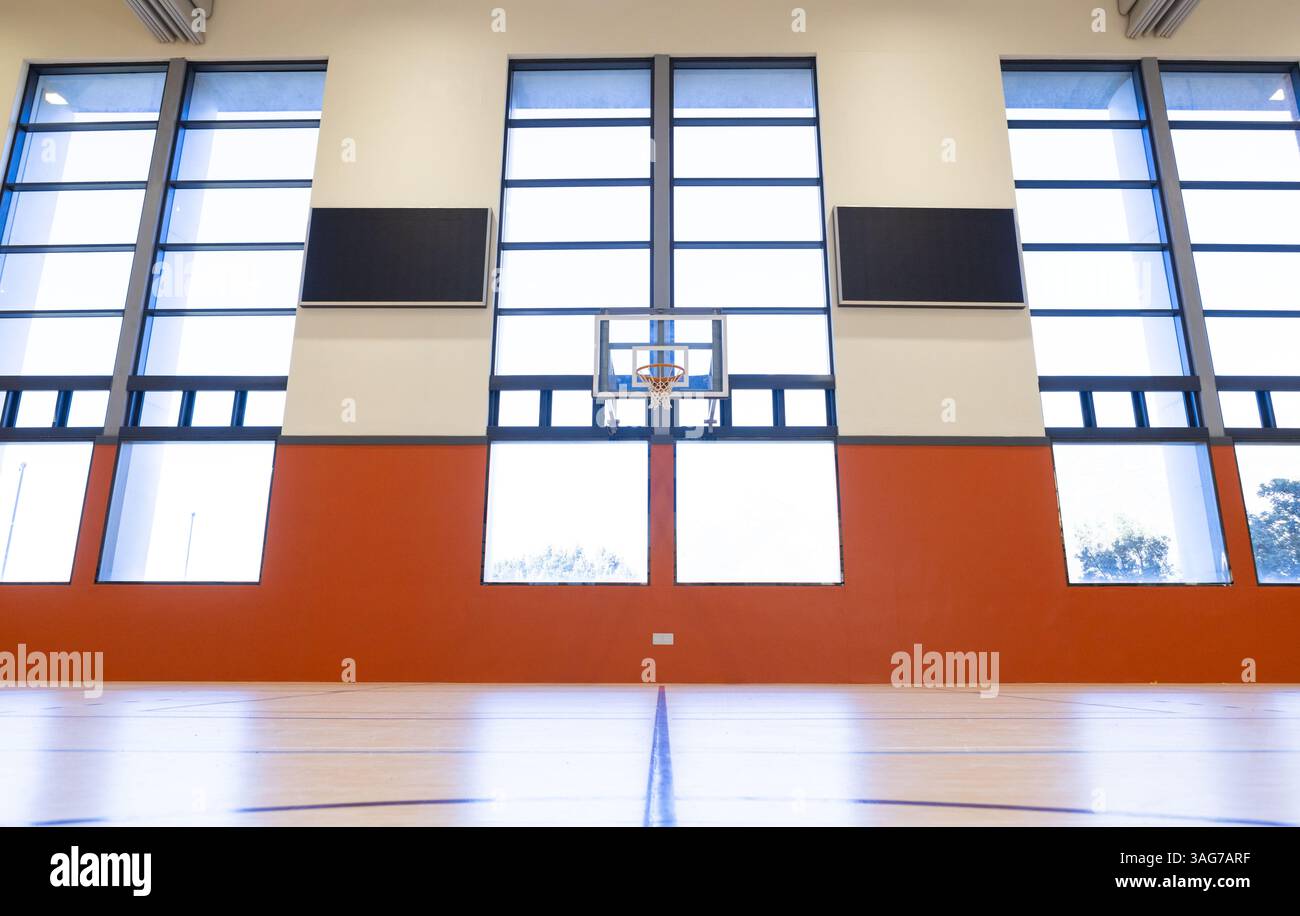 Basketballkorb in leerem Schulgymnasium mit großen Fenstern und hoher Decke Stockfoto