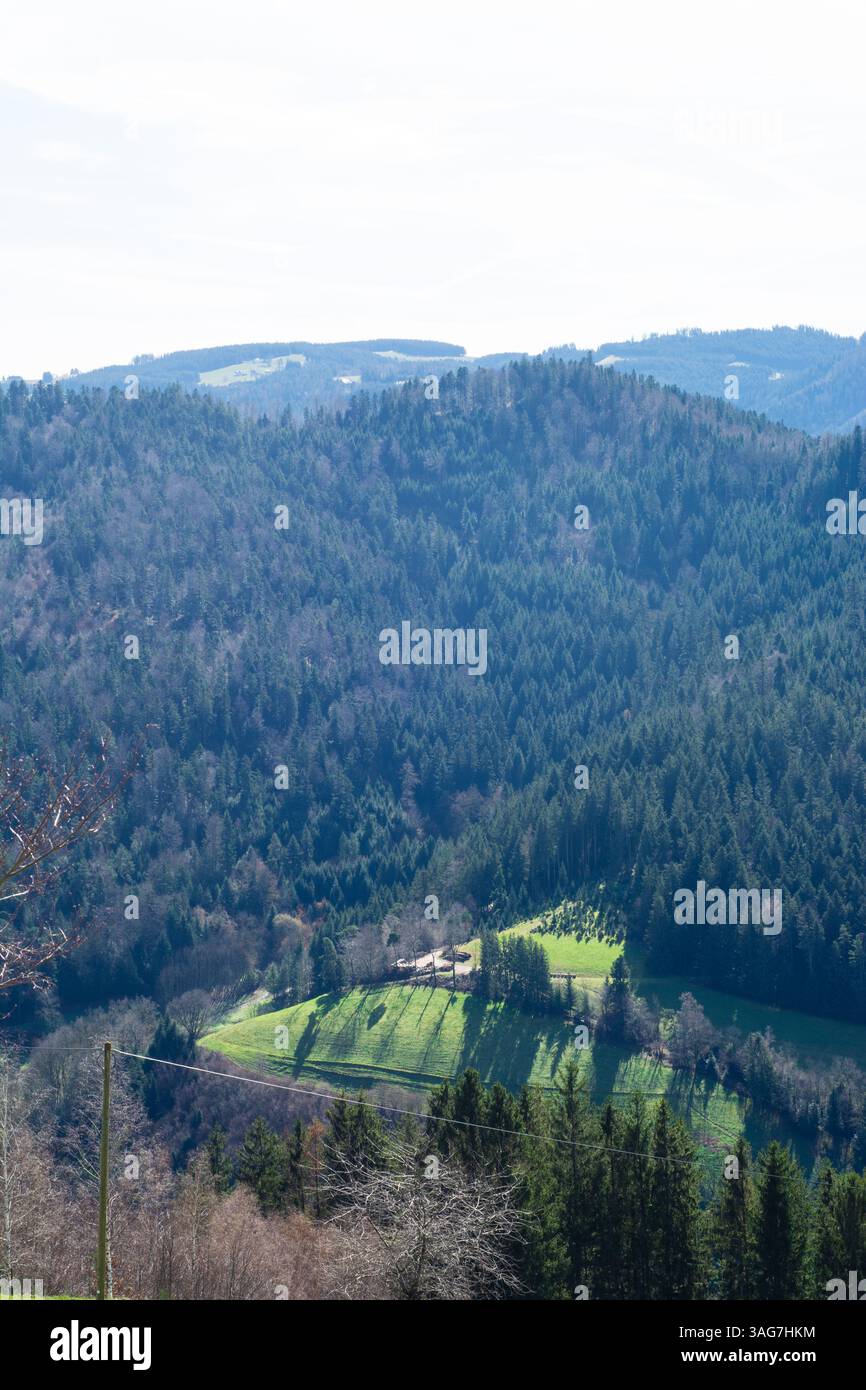 Üppige grüne Felder erstrecken sich über den Talboden, eingebettet zwischen hoch aufragenden Bergen, während das Sonnenlicht auf der Landschaft tanzt und eine malerische Atmosphäre schafft Stockfoto