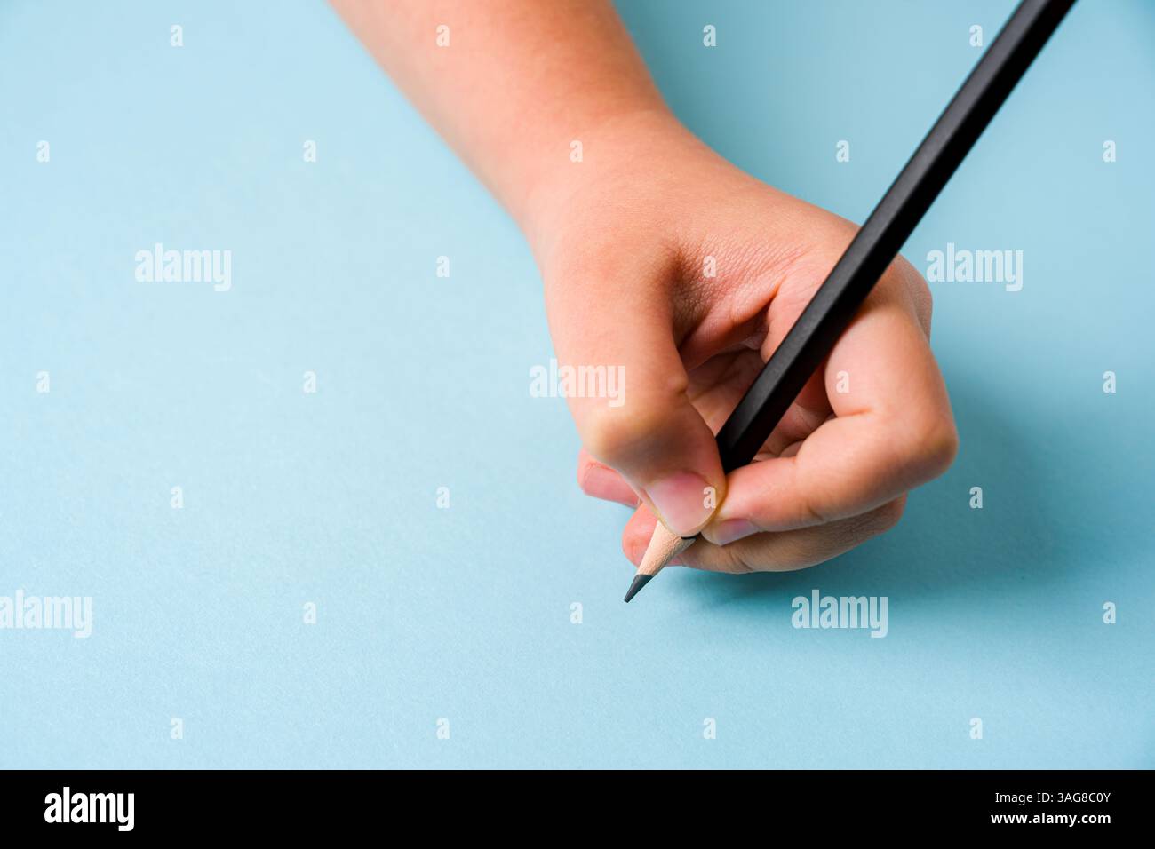 Die linke Hand hält einen Kugelschreiber auf einem offenen Notizbuch auf blauem Hintergrund Stockfoto
