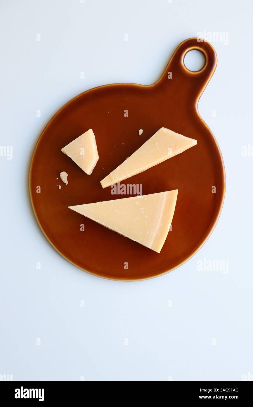 Hartkäse-Keile auf brauner Keramikplatte mit minimalem Hintergrund Stockfoto