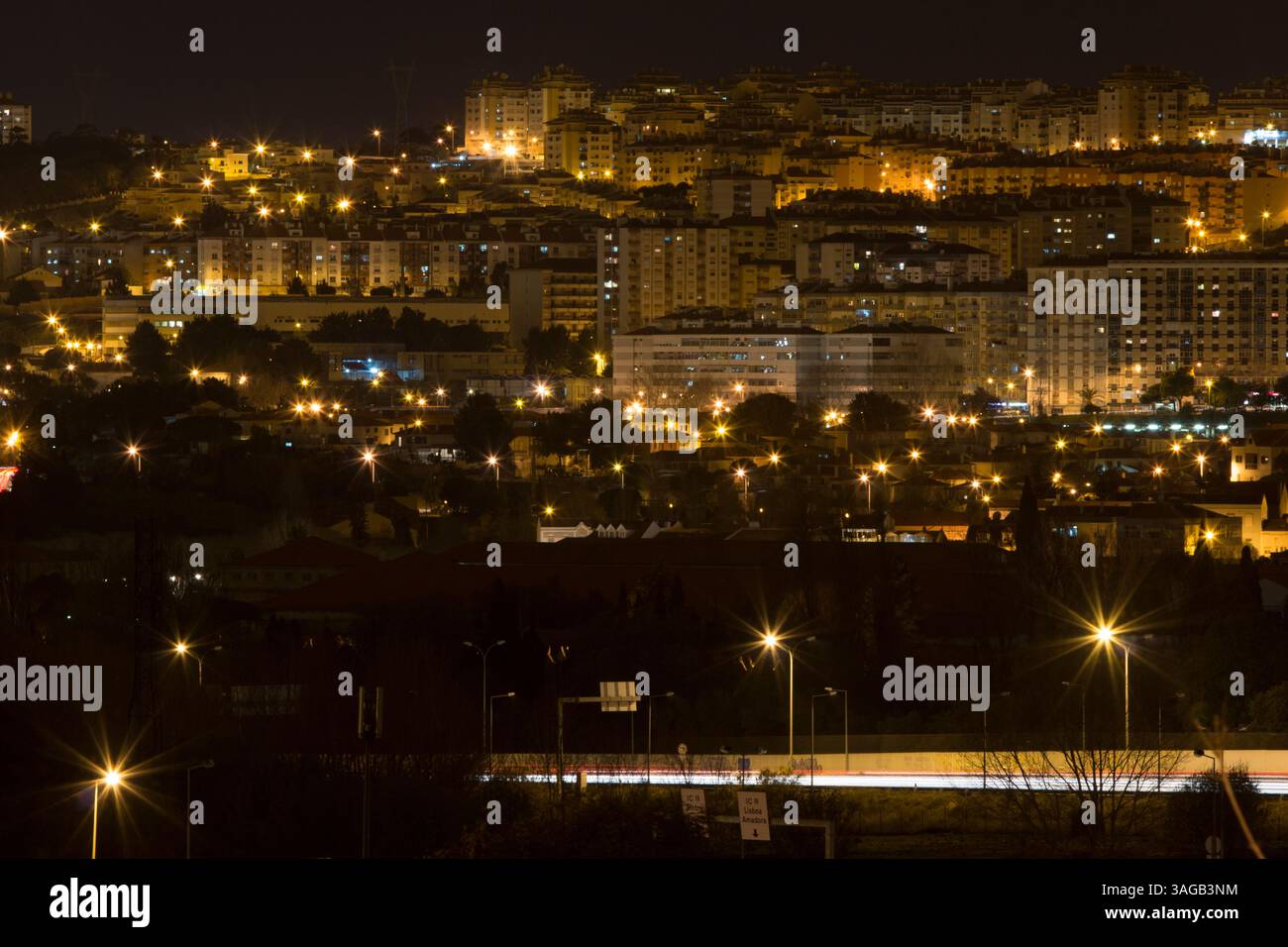 Nächtliches Stadtbild von Queluz, Portugal, mit leuchtenden Straßenlaternen und Wohnhäusern unter dunklem Himmel. Stadtlichter sorgen für einen wunderschönen Bokeh-Effekt. Stockfoto