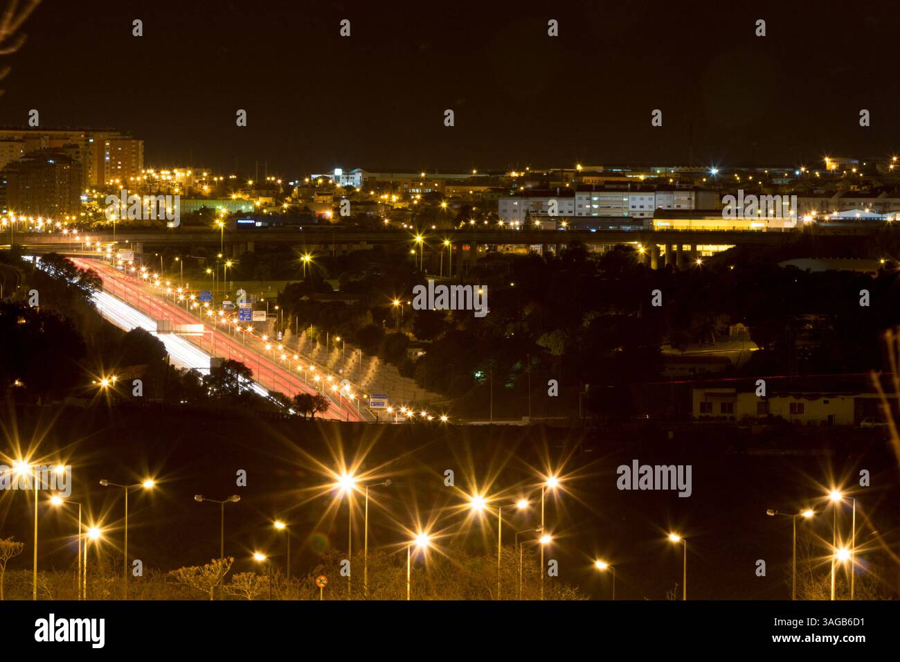 Nächtliches Stadtbild von Queluz, Portugal, mit leuchtenden Straßenlaternen und Wohnhäusern unter dunklem Himmel. Stadtlichter sorgen für einen wunderschönen Bokeh-Effekt. Stockfoto