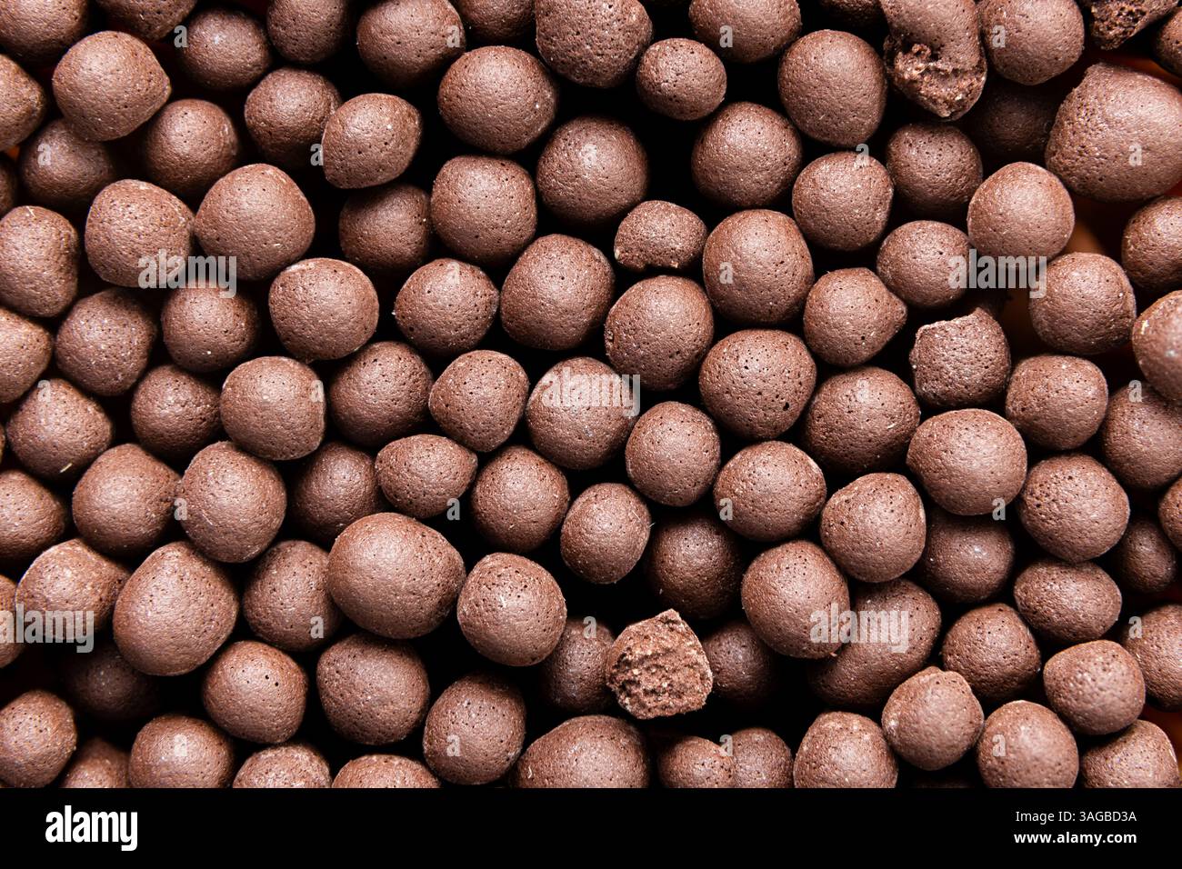 Dieses Makrofoto zeigt ein eng gepacktes Muster aus kleinen braunen Kugeln, die entweder knusprigen Schokoladen-Müslikugeln oder Holzköpfen ähneln Stockfoto