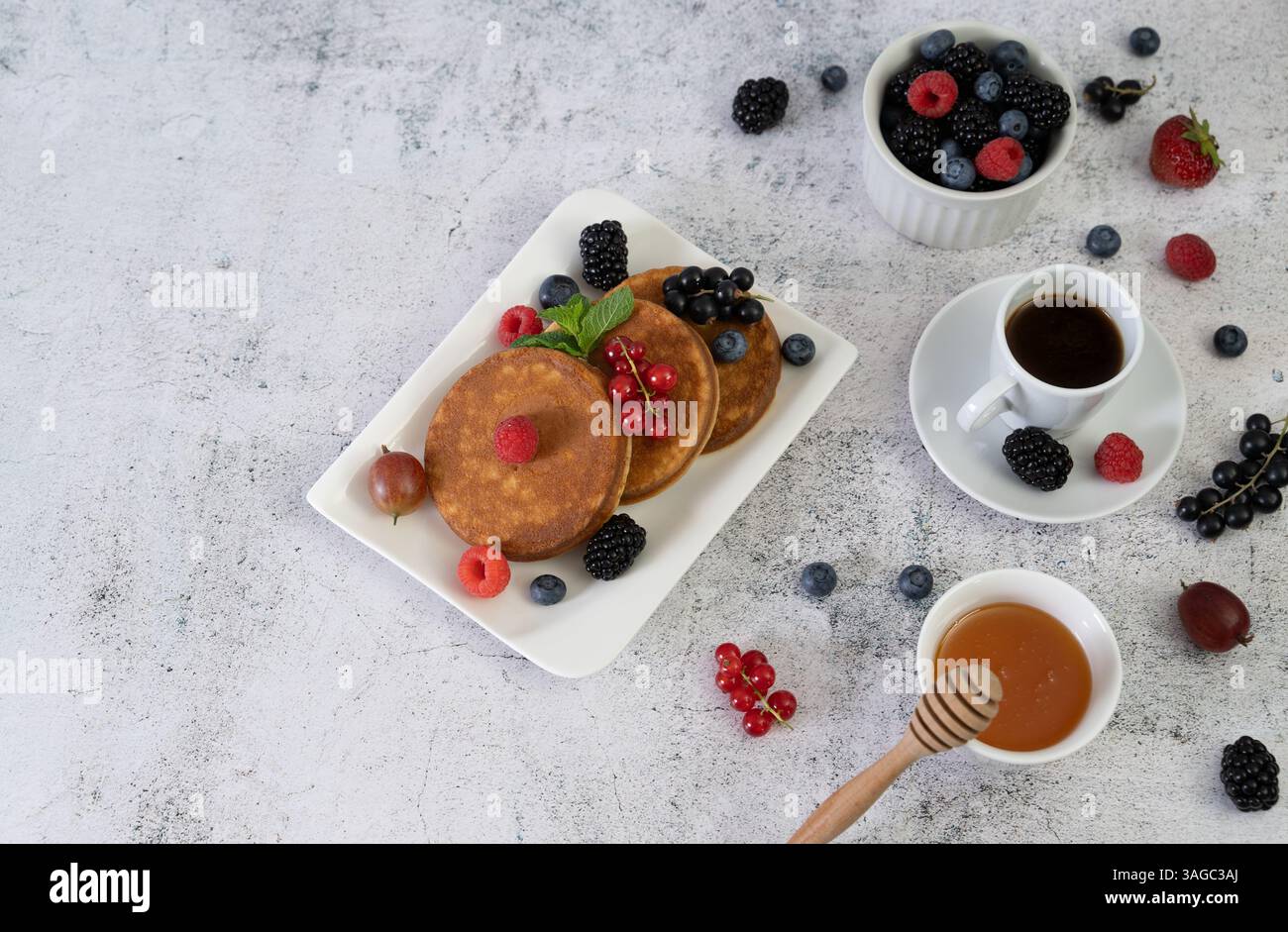 Goldbraune Pfannkuchen mit frischem Obst, elegant auf einer weißen quadratischen Schale über einer grauen Tischplatte angeordnet Stockfoto