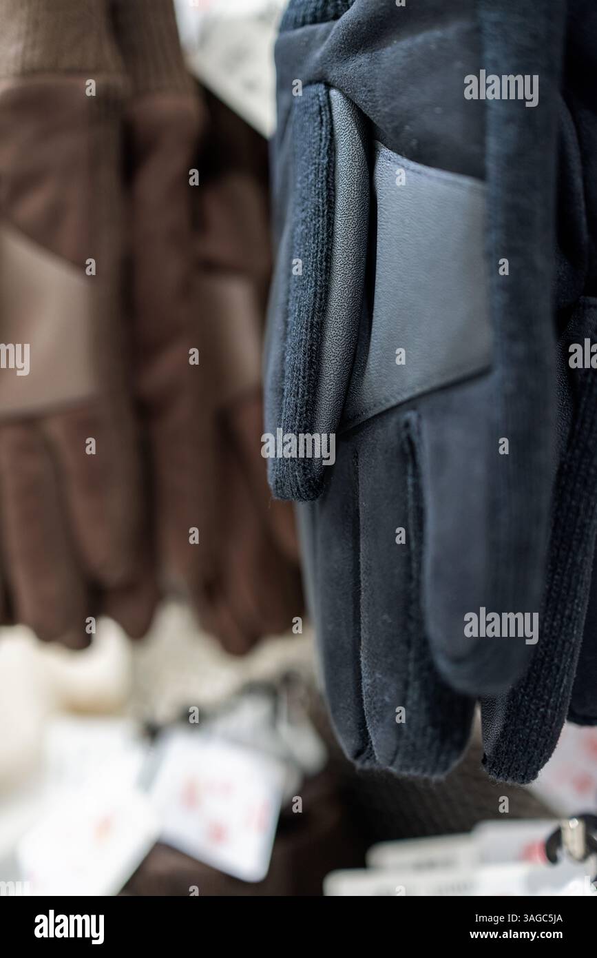Nahaufnahme von schwarzen und braunen Winterhandschuhen mit Stoff- und Lederelementen, die in einem Geschäft hängen und Texturnähte und strapazierfähige Materialien hervorheben Stockfoto