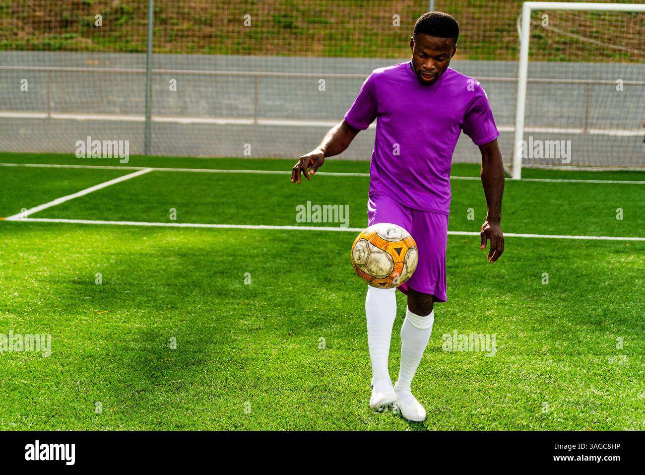 Porträt eines jungen, lächelnden schwarzen afrikaners, der während des Trainings auf einem Fußballfeld läuft und spielt, glücklich aussieht. Junger Sportler, der in einer Socce trainiert Stockfoto