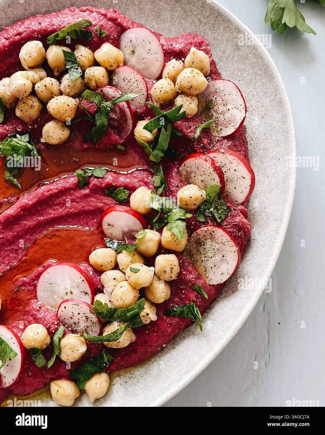 Lebendiger Rote-Bete-Hummus auf einer rustikalen Keramikplatte serviert, garniert mit Kichererbsen, frischen Rettichscheiben, gehackten Kräutern und einem Hauch Olivenöl. Stockfoto