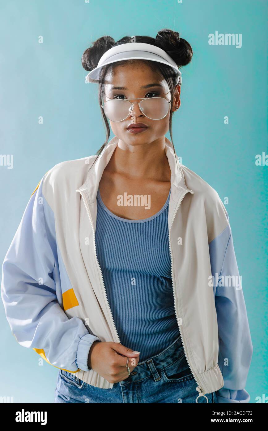 Junge Frau in Retro-Jacke und Visier posiert selbstbewusst vor blauem Hintergrund. Mode, Style, Vintage, trendig, lebendig Stockfoto