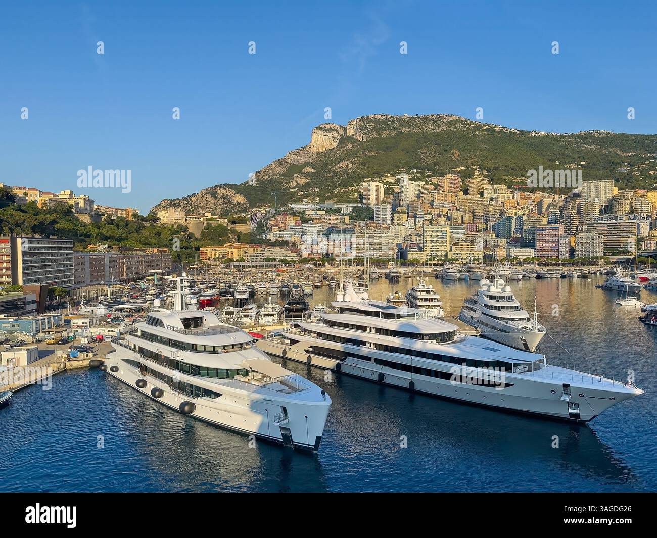 Fürstentum Monaco, Frankreich - 9. Juli 2024: 3 superreiche Yachten vor dem Hafen mit Stadtbild des urbanen Dschungels hinten und oben auf der Maritimen Alpes m Stockfoto