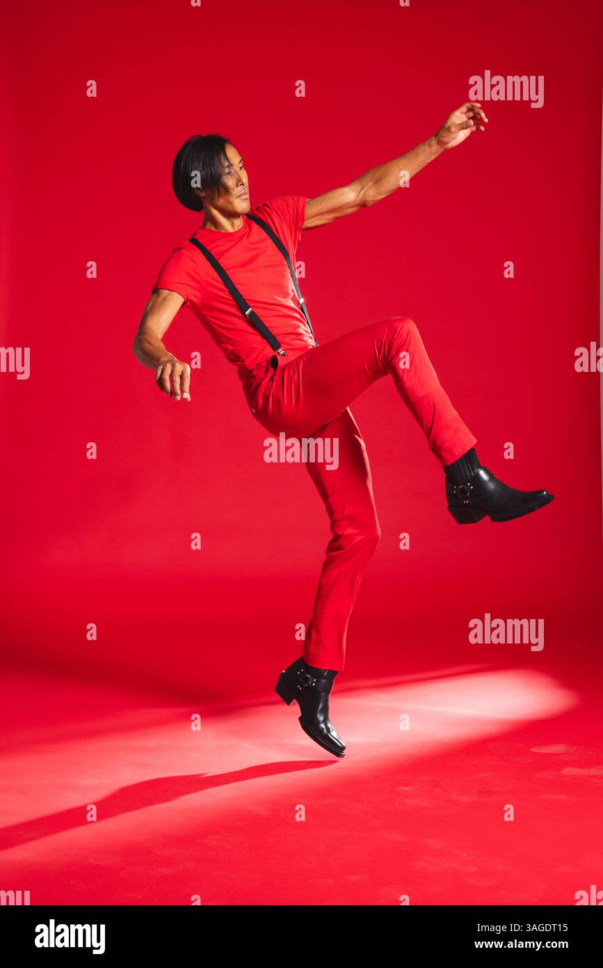Mann in rotem Outfit tanzt energisch im Studio und drückt Freude und Bewegung aus. Tanz, Choreographie, Performance, Ausdruck, dynamisch, Glück Stockfoto