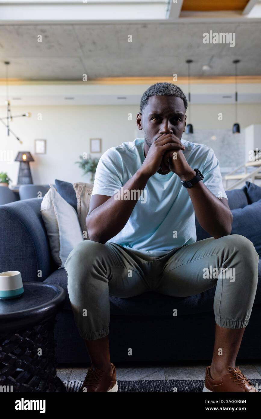 Ein nachdenklicher Afroamerikaner sitzt zu Hause auf dem Sofa und denkt mit gefesselten Händen nach. Kontemplation, Introspektion, Entspannung, Ruhe, Soli Stockfoto
