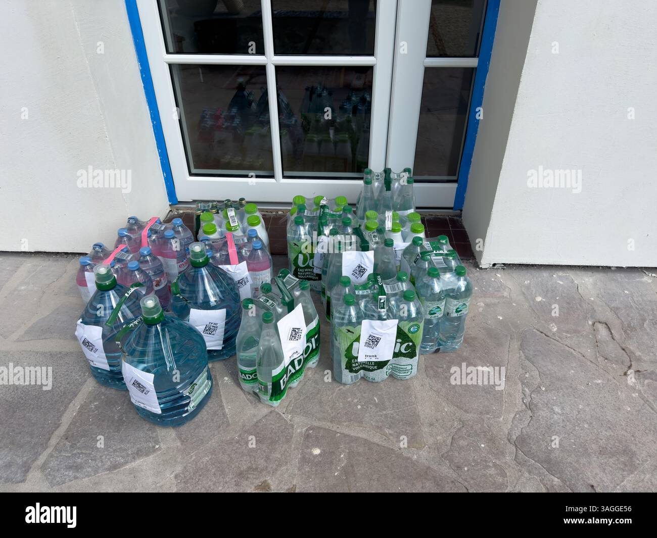 Sammlung von Wasser in Flaschen, die tagsüber bei Sonnenlicht vor einem Gebäudeeingang angeordnet sind Stockfoto