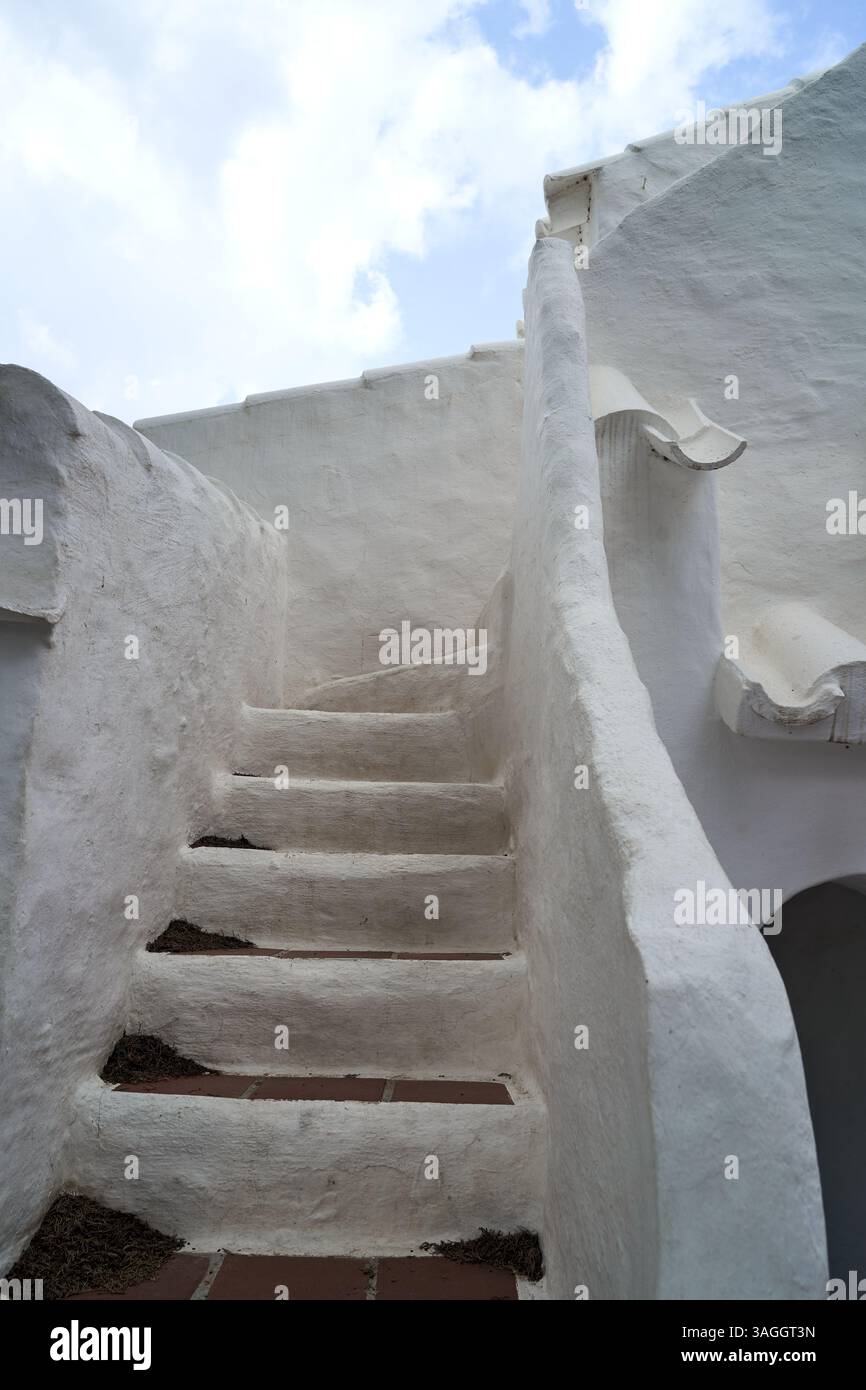 Ein bezaubernder Blick auf die weiße Treppe in Binibeca, Menorca, die vor dem Hintergrund eines blauen Himmels nach oben führt. Die Architektur zeichnet sich durch ein einzigartiges Design aus. Stockfoto
