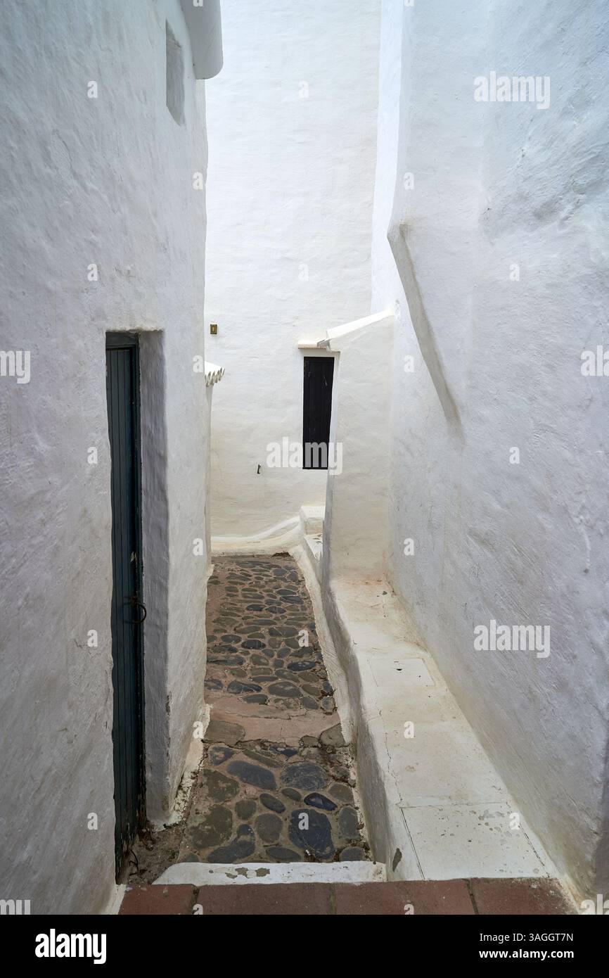 Eine schmale, weiß getünchte Gasse in Binibeca, Menorca, mit Kopfsteinpflaster und dunklen Türen, die eine ruhige und malerische Aussicht bieten. Stockfoto
