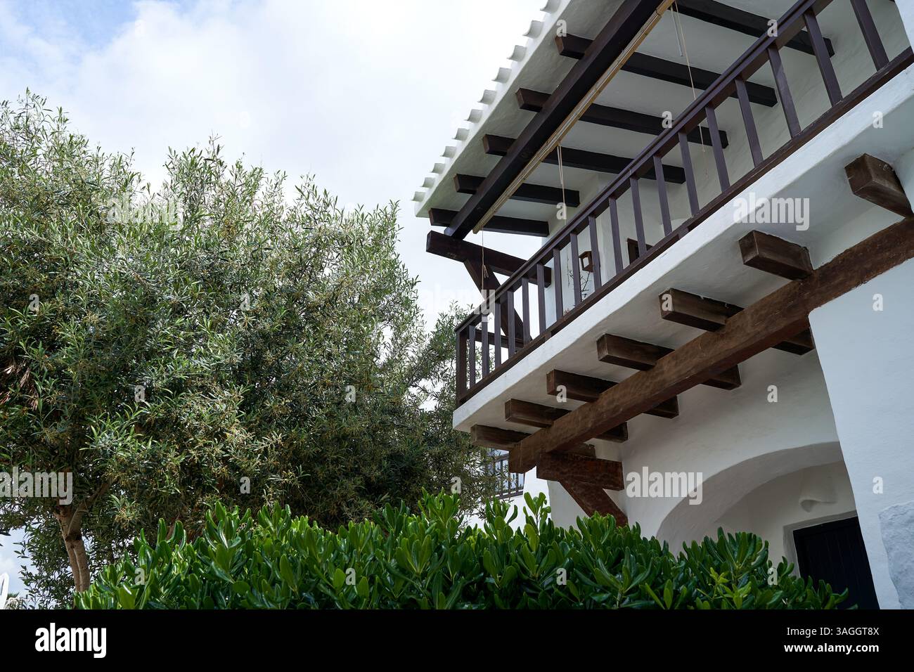Eine schöne Villa in Binibeca, Menorca, verfügt über einen Balkon mit Holzbalken und einem üppig grünen Baum. Stockfoto