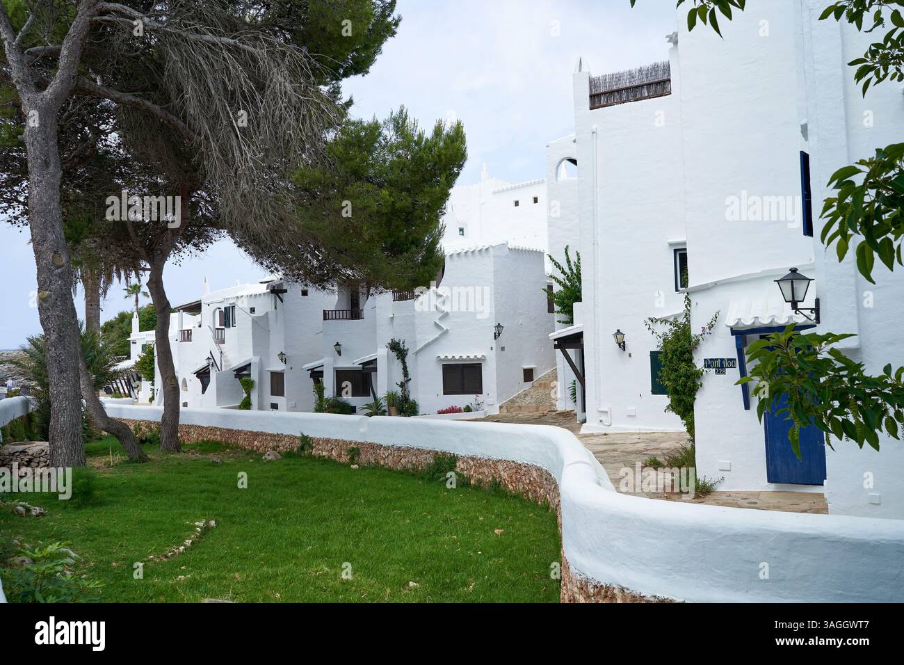 Blick auf die traditionelle Architektur in Binibeca, Menorca, mit weißen Gebäuden und Grünflächen an einem sonnigen Tag. Stockfoto