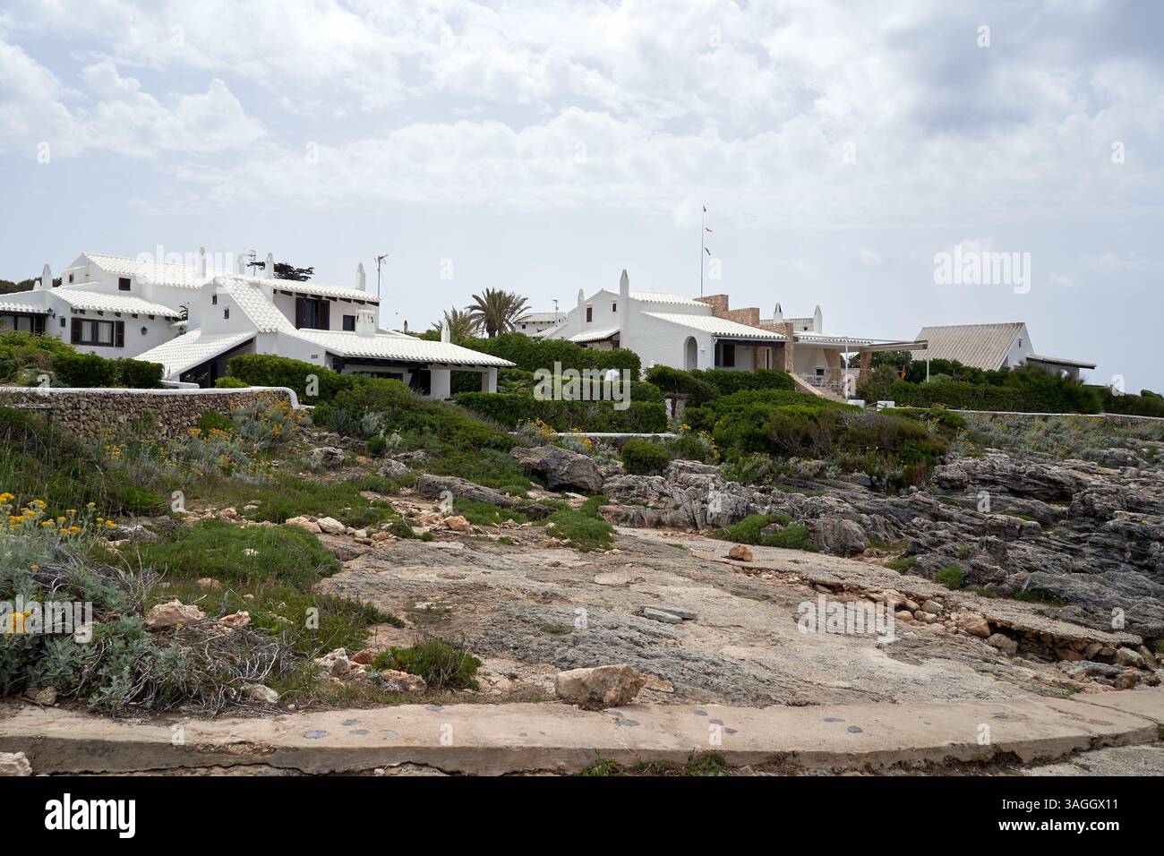 Malerischer Blick auf weiß getünchte Villen in Binibeca, Menorca, Spanien. Die Architektur ist charakteristisch für die Balearen mit üppigem Grün und Wolken Stockfoto
