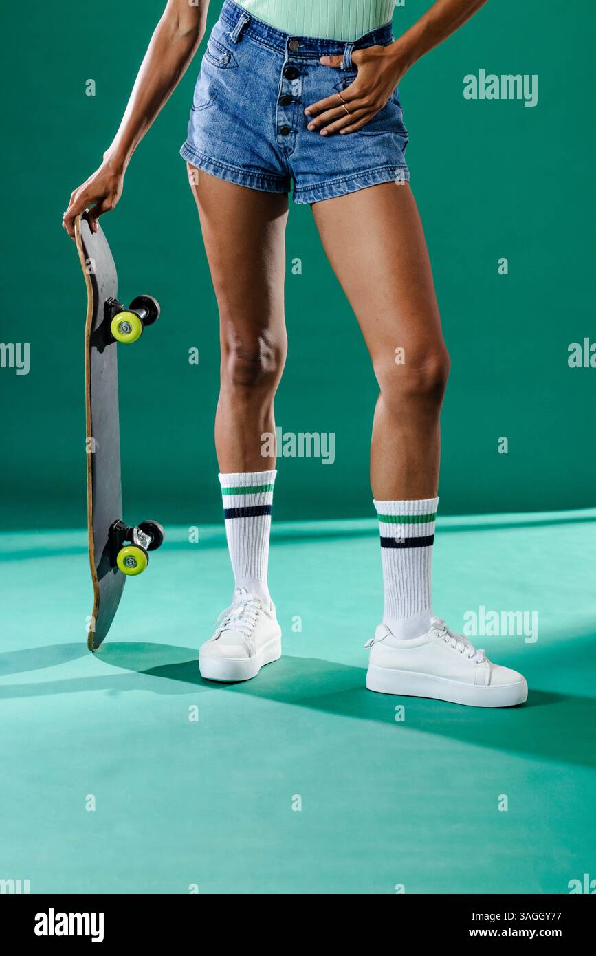 Person mit Skateboard in Jeansshorts und Sneakers, bereit für Action. Skateboarding, Lifestyle, Streetwear, Urban, Freizeit, aktiv Stockfoto