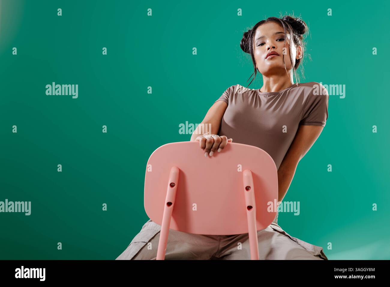Selbstbewusste Frau, die auf rosafarbenem Stuhl in stilvollem Grunge-Studio sitzt. Mode, Selbstvertrauen, Innenausstattung, Trend, Alternative, städtisch Stockfoto