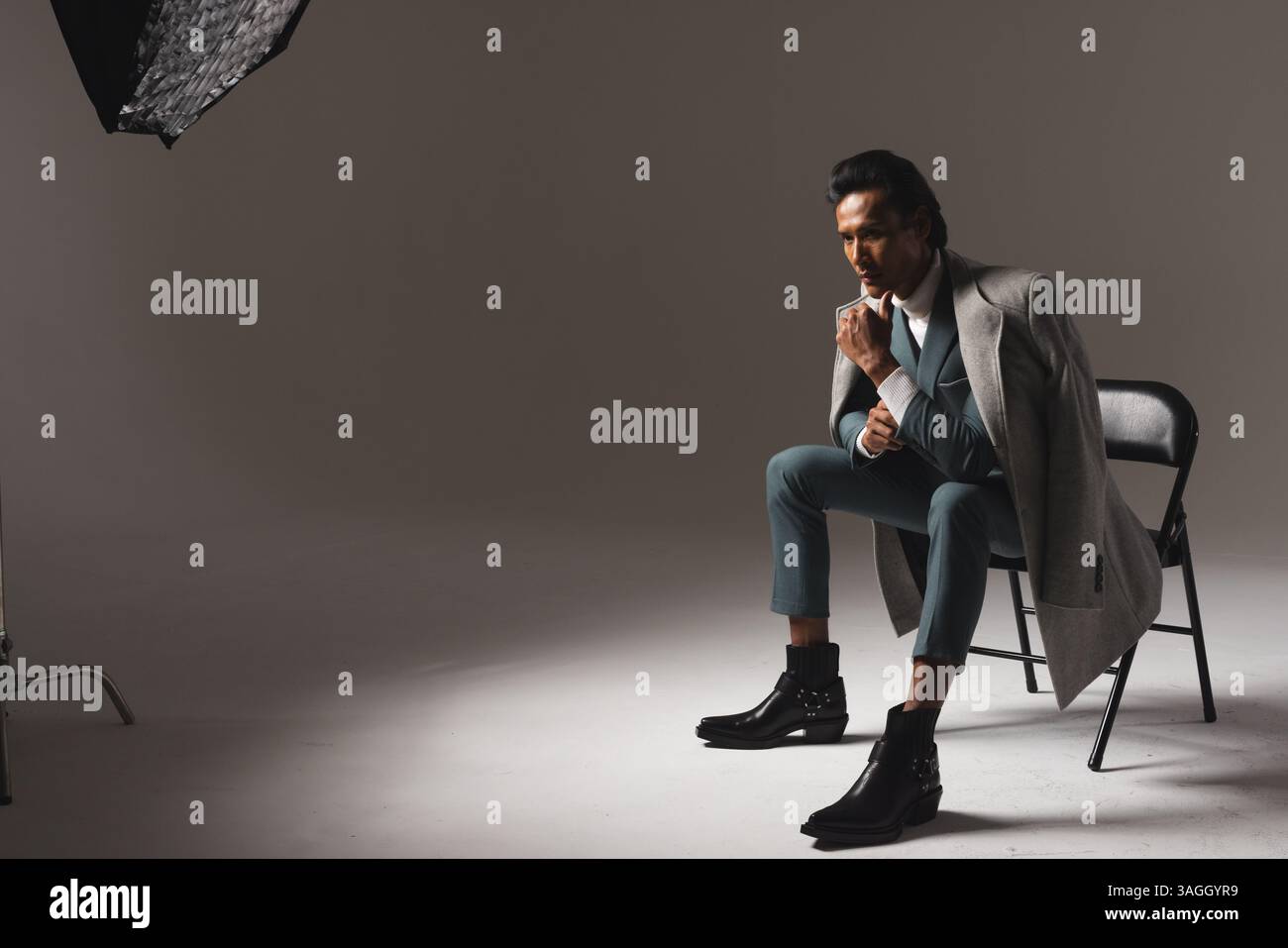 Stilvoller Mann in Anzug und Mantel, der auf einem Stuhl sitzt und im Studio nachdenkt. Mode, Stil, Business, Kontemplation, Eleganz, Herrenbekleidung Stockfoto