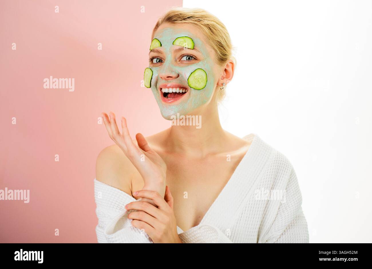 Lächelnde Frau mit Tonkosmetik-Gesichtsmaske und frischen Gurkenscheiben im Gesicht im Spa-Salon. Kosmetologie, Dermatologie, Hautpflege und kosmetische Verfahren. Stockfoto